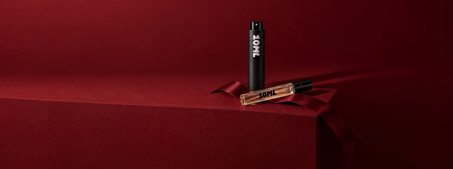 A 10ML atomiser and a filled sample vial on a claret plinth with a satin ribbon