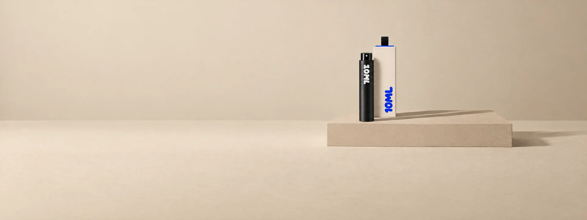 A black 10ML atomiser beside its cream box on a sand-coloured plinth