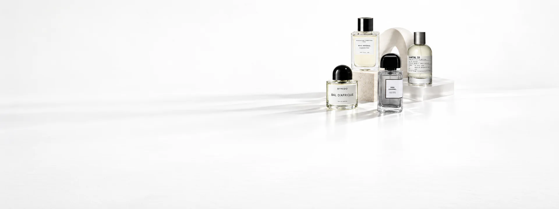 Byredo Bal d’Afrique, Essential Parfums Bois Impérial, BDK Gris Charnel and Le Labo Santal 33 bottles on pale stone